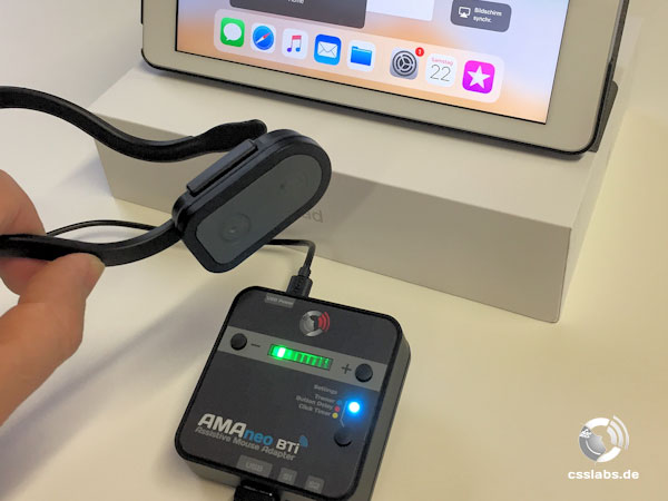 AMAneo BTi. Photo of an iPad connected via blue-tooth to an AMAneo BTi square box, and head-controlled mouse.