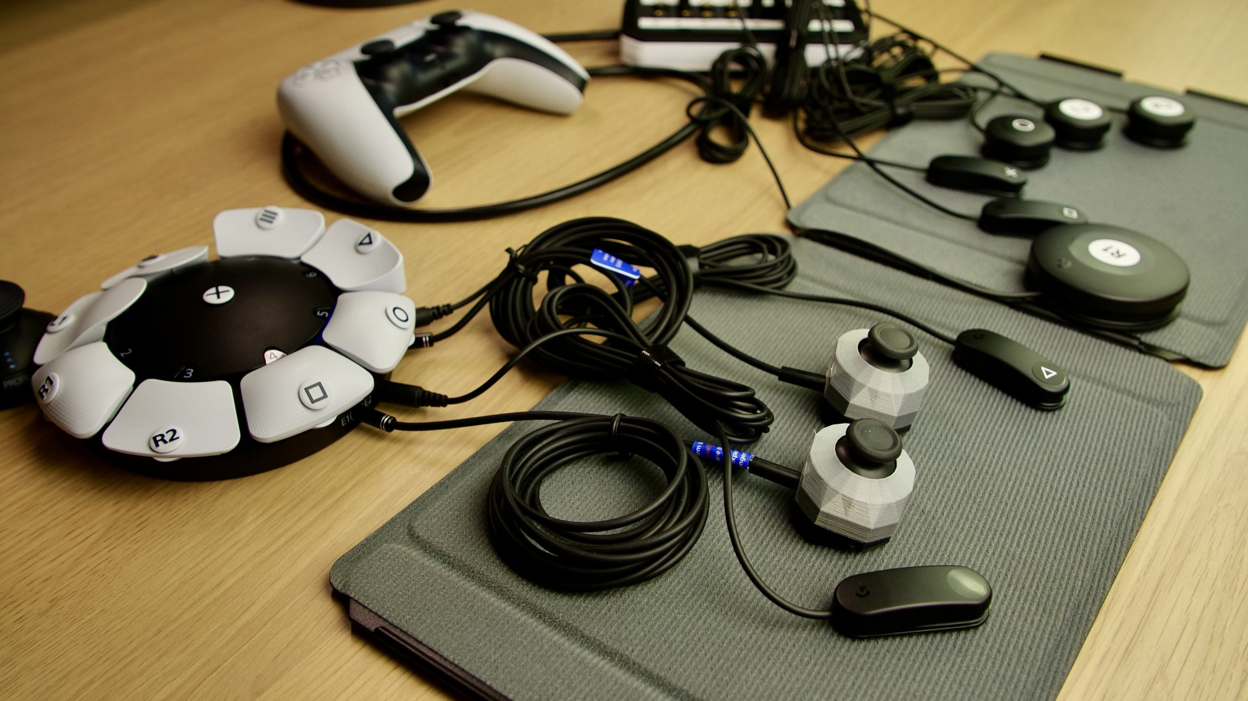 Photo showing the 19-switch DualSense interface with a Sony Access controller alongside it and 8 switches connected to both (2 into the access controller and 6 into the 19-switch DualSense interface. Two external Celtic Magic joysticks are also connected to the Access controller. The joysticks and switches are placed on two Logitech G hook and loop boards.