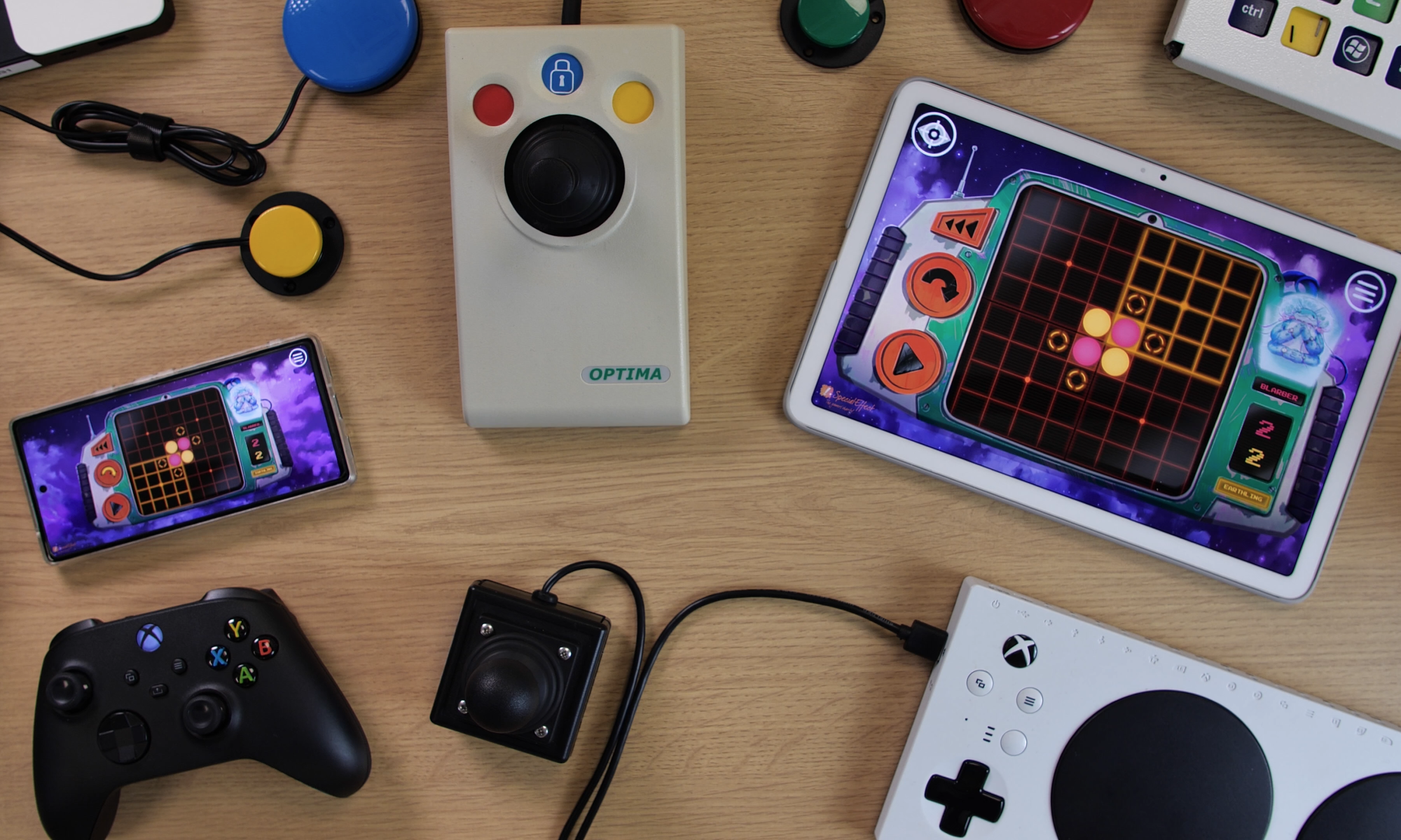 Photo showing an Android smartphone and a tablet with the game 'Othello' open on them. The devices are surrounded by devices including an Xbox Adaptive coController, and Optima Joystick, an Xbox controller and some accessibility switches.