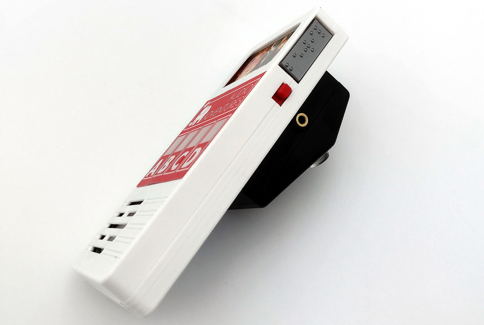 Side view with on/off switch and braille side of inserted cartridge. On the rear a black box with switch socket for the D button.