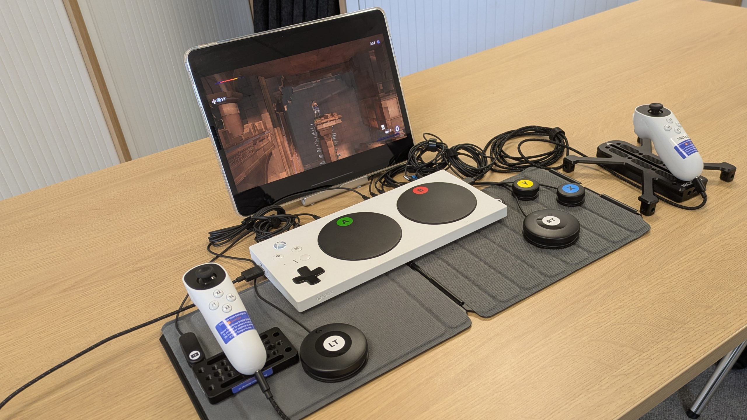 Photo of an Xbox Adaptive Controller with joysticks and switches connected  in front of an iPad Pro with Prince of Persia: the Lost Crown running on it.