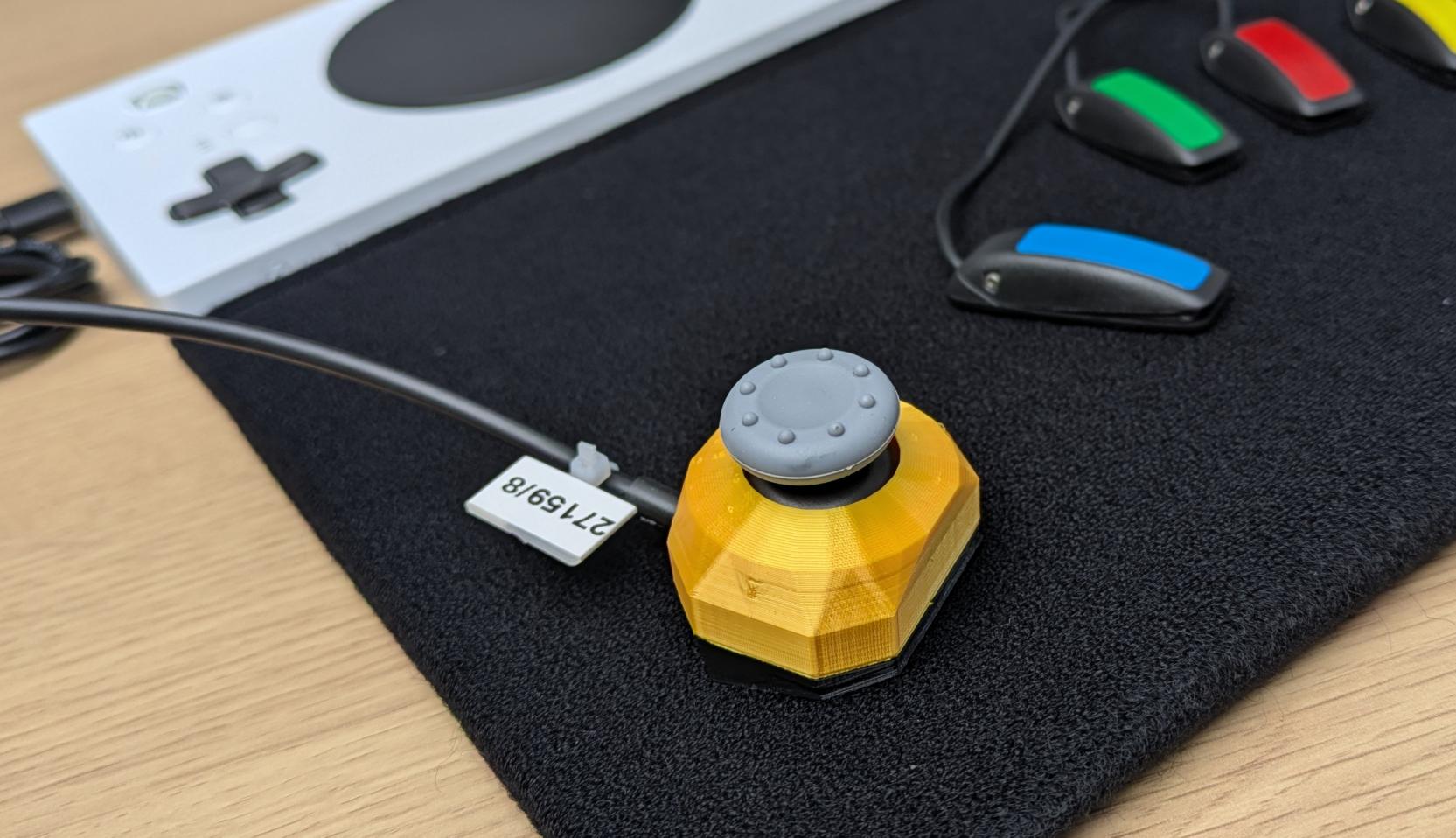 Photoof a J3 Compact version of the Very Light Force JN Mini Joystick alongside four Atec Ultra Ligh HD switches on on a TechPad tray. An XAC is in the background which these are all plugged into. 