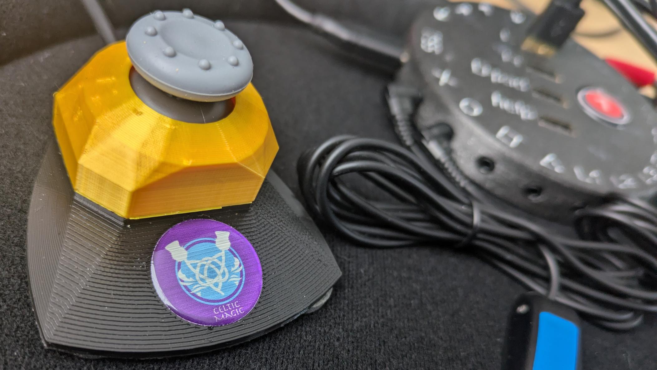 Photo of a J2 Desktop base Very Light Force JN Mini Joystick connected to a Catch 22 PS5 interface in the background. An Ultra Light HD switch from Atec is also connected. They are mounted on a Trabasack tray.