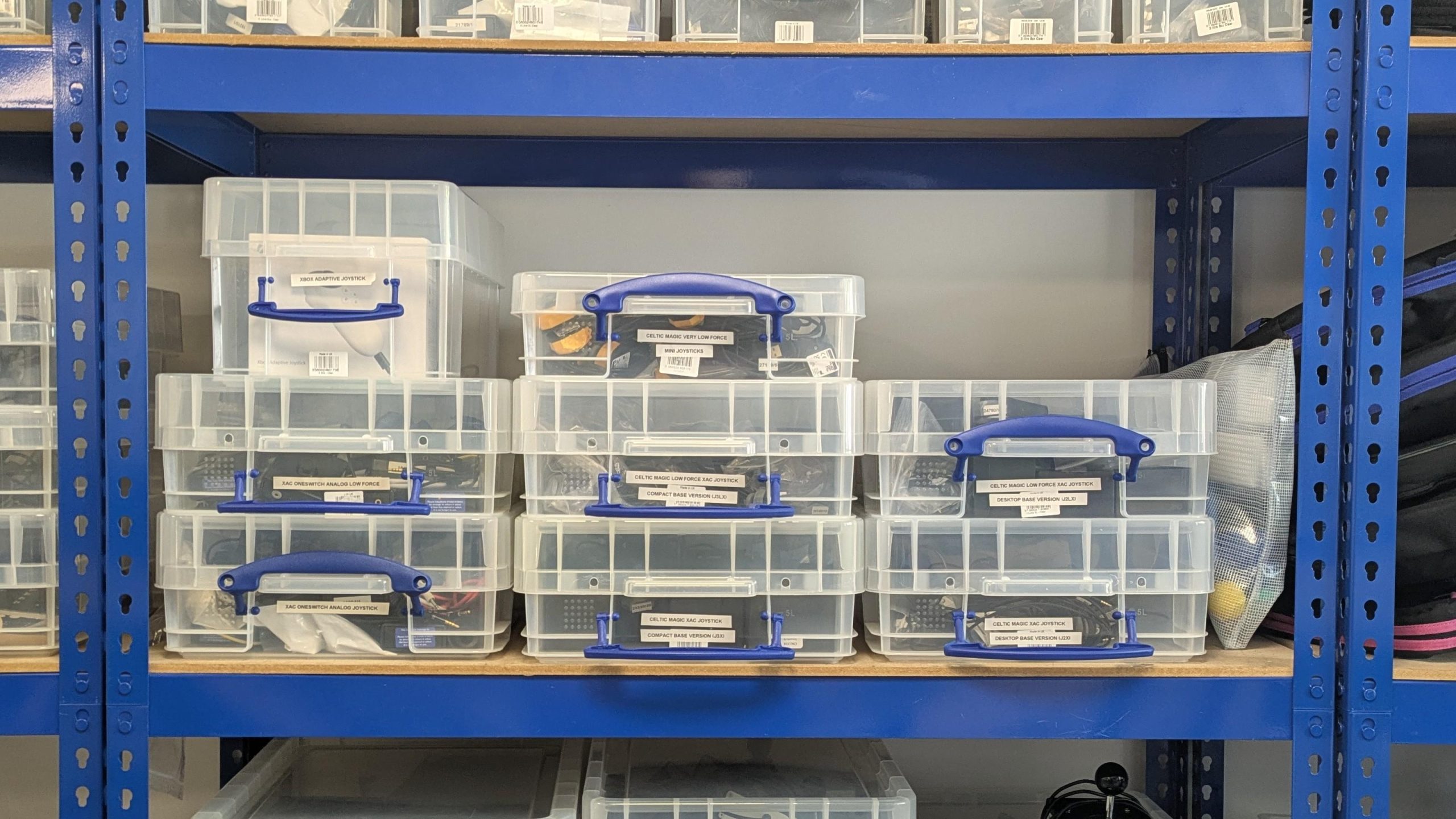 Photo showing  some clear labelled boxes stacked on shelving. Inside are a variety of different joysticks.